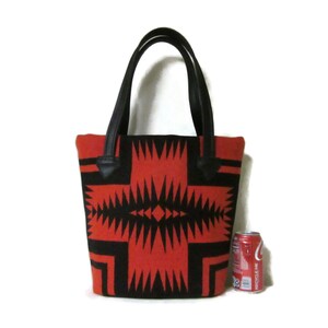May include: A red and black tote bag with a geometric pattern. The bag has black leather handles and is about the size of a can of soda.