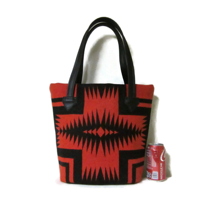 May include: A red and black tote bag with a geometric pattern. The bag has black leather handles and is about the size of a can of soda.
