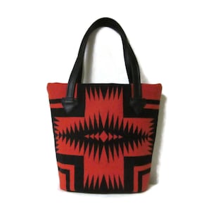 May include: A red and black tote bag with a geometric pattern. The bag has black leather handles.