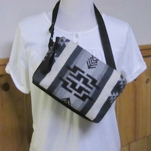 May include: A black and white patterned crossbody bag with a black strap. The bag is made of woven fabric and has a geometric design.