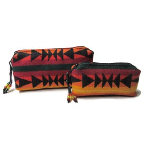 May include: Two zippered pouches with a geometric pattern in shades of red, orange, green, and black. The pouches have black zippers and beaded pull cords. The larger pouch is in the background, and the smaller pouch is in the foreground.