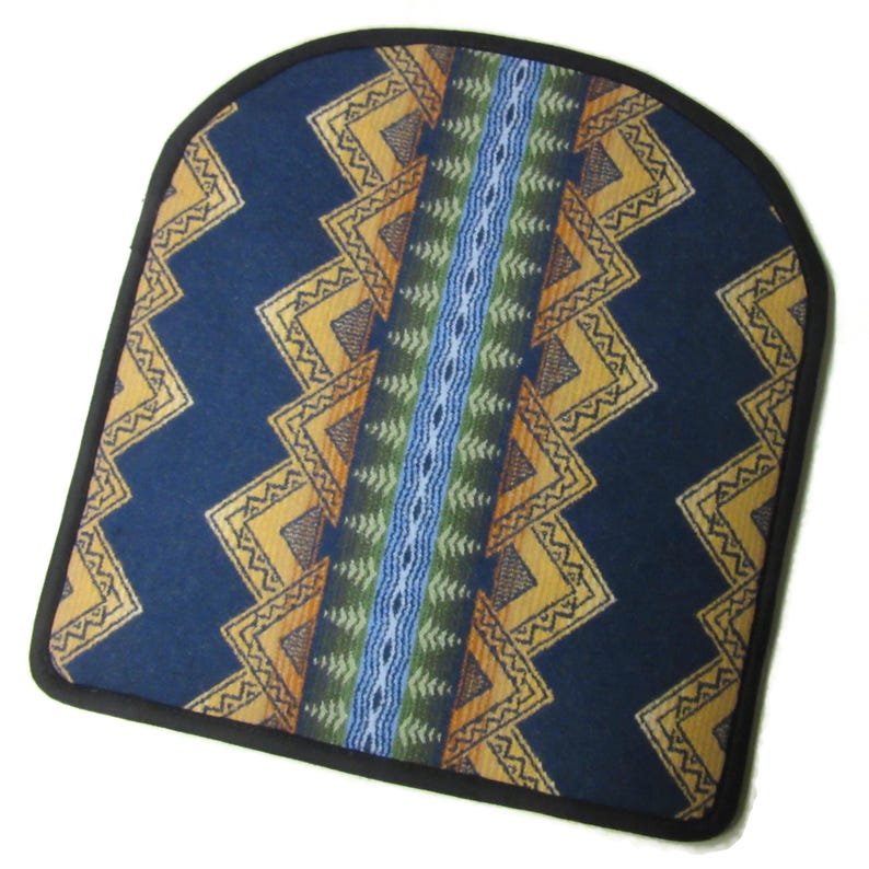 May include: A navy blue seat cushion with a geometric pattern in yellow, orange, green, and blue. The cushion has a black border and a central vertical stripe design. The overall shape is rounded at the top.