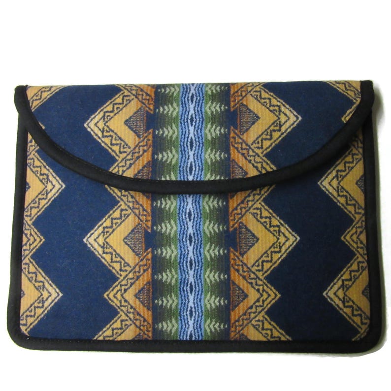 May include: A rectangular, navy blue laptop sleeve with a flap closure. The sleeve features a geometric pattern in shades of gold, orange, green, and blue. The edges are trimmed with black piping, creating a clean, finished look.