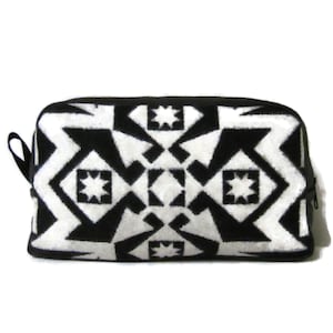 May include: A rectangular black and white patterned cosmetic bag. The bag features a geometric design with star and diamond shapes. It has a black zipper and a small black loop on the side.