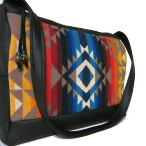 May include: A black shoulder bag with a geometric patterned front panel in shades of red, blue, orange, and beige. The bag has a black leather strap and trim, and a drawstring with decorative beads.
