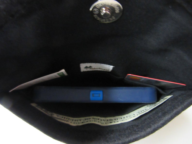 May include: The inside of a black purse with a silver snap closure. The purse contains a blue fitness tracker, a credit card, a piece of paper with the words "Save 10%" and a small tag with the word "Mountain" on it.