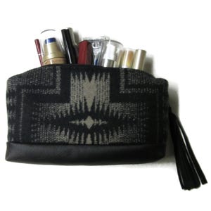 May include: A black and gray patterned cosmetic bag with a black leather bottom and a black tassel. The bag is filled with various cosmetic products, including lipsticks, mascaras, and lotions.
