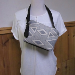 May include: A gray and white patterned crossbody bag with a black adjustable strap. The bag is made of a soft, woven fabric and has a zipper closure.