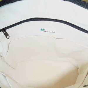 May include: The inside of a white canvas tote bag with a black zipper and a green logo that says "Timberline Ltd."