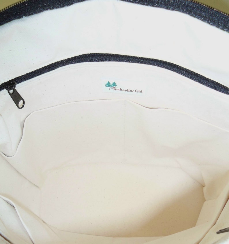 May include: The inside of a white canvas tote bag with a black zipper and a green logo that says "Timberline Ltd."