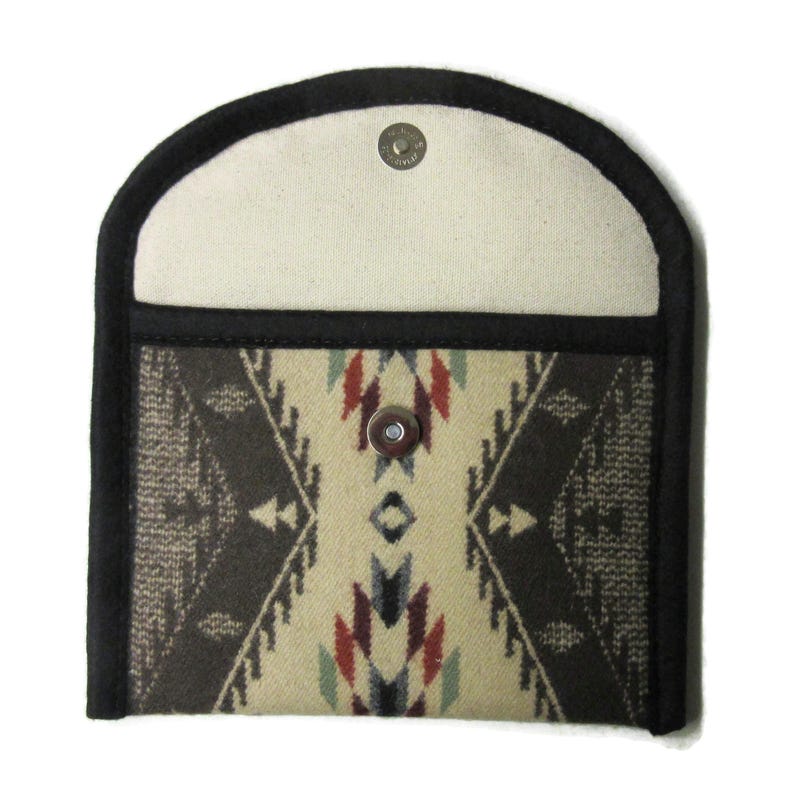 May include: A small, open wallet with a Southwestern pattern. The wallet has a black border and a cream-colored interior. The patterned section features a geometric design in shades of brown, red, and cream. A metal snap closure is visible.