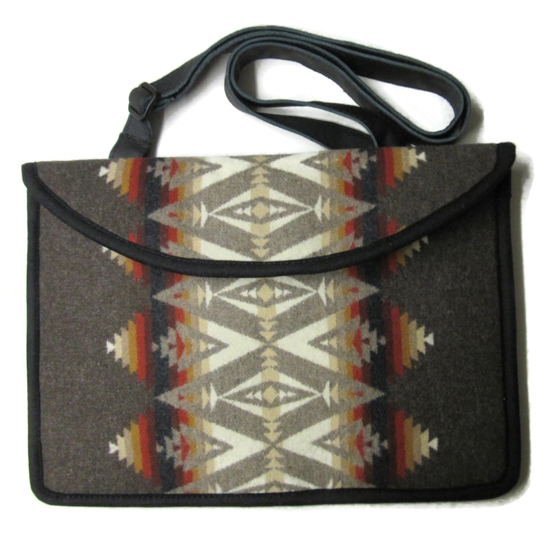 May include: A rectangular shoulder bag with a geometric pattern in shades of brown, beige, red, and yellow. The bag has a black trim and a gray adjustable strap. The flap closure is curved.