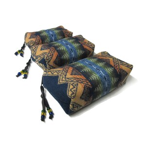 May include: Three blue, tan, and orange patterned fabric rectangular pillows with black tassels and colorful beads.