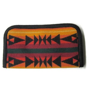 May include: A rectangular, patterned case with a black border. The case features a geometric design with black triangles and horizontal stripes in shades of orange, red, and green. The case is likely made of fabric.