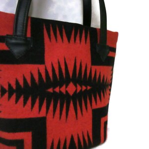 May include: Red and black tote bag with a geometric pattern. The bag has black leather handles.