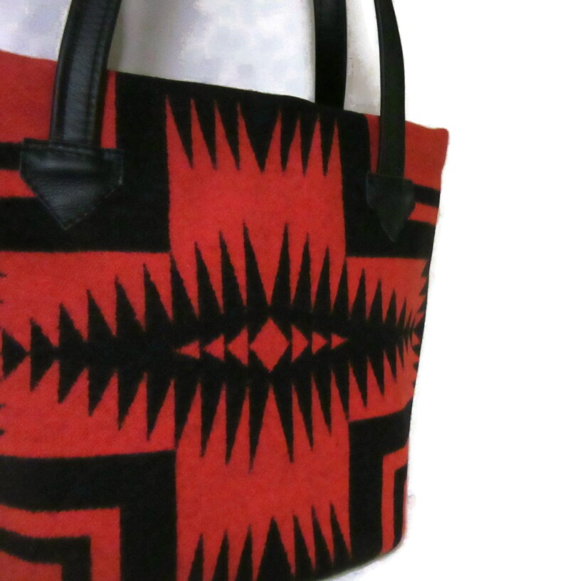 May include: Red and black tote bag with a geometric pattern. The bag has black leather handles.