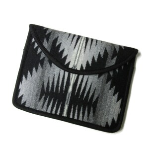 May include: Black and grey patterned clutch bag with a black border. The pattern is geometric and resembles a Native American design.