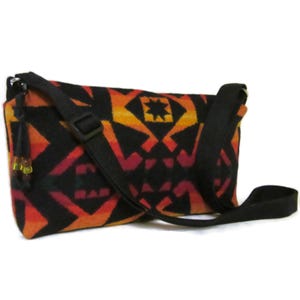 May include: A black crossbody bag with a colorful geometric pattern in shades of orange, red, and yellow. The bag has a black adjustable strap and a flap closure.