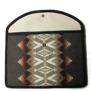 May include: A rectangular, gray felt case with a geometric pattern in cream, orange, and red. The case has a cream-colored flap with a snap closure and a black border. The design is reminiscent of Native American textiles.