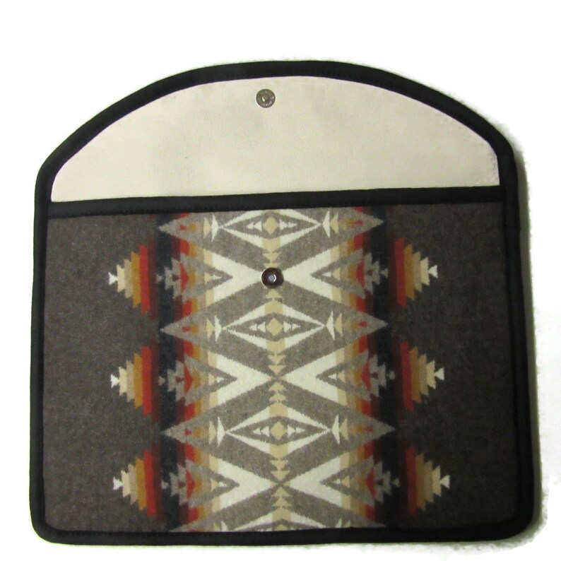 May include: A rectangular, gray felt case with a geometric pattern in cream, orange, and red. The case has a cream-colored flap with a snap closure and a black border. The design is reminiscent of Native American textiles.