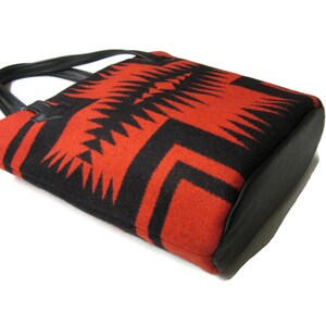 May include: A red and black tote bag with a geometric pattern. The bag has a black leather handle and base.