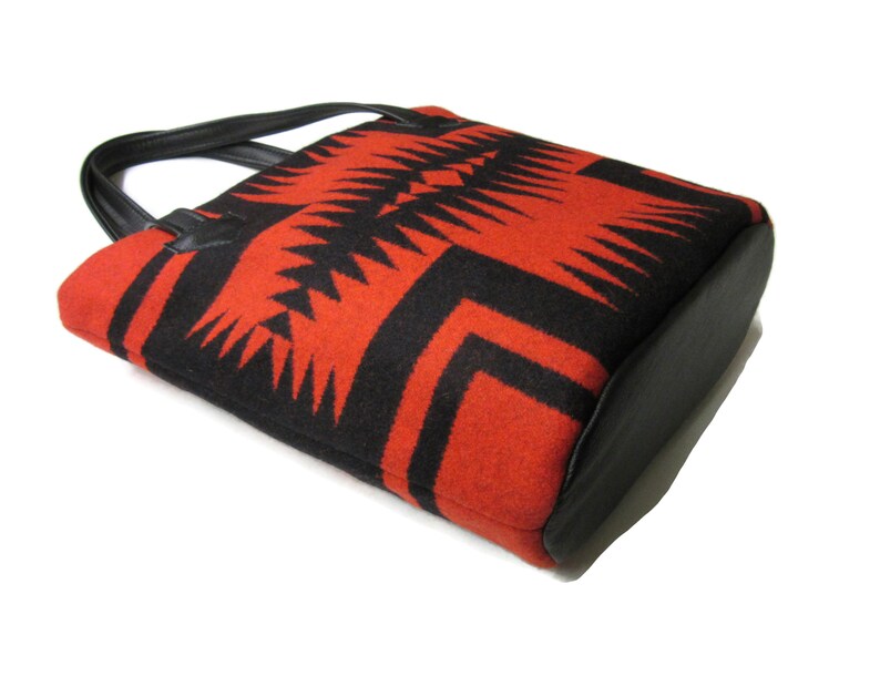 May include: A red and black tote bag with a geometric pattern. The bag has a black leather handle and base.