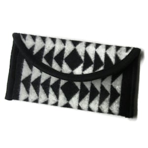 May include: A black and white geometric pattern adorns a rectangular clutch. The clutch features a flap closure with a black trim. The design consists of black diamonds and triangles against a white background, creating a striking visual contrast.