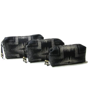May include: Three black and white patterned zippered pouches of different sizes. The pouches have a geometric design and are made of a soft, textured fabric.