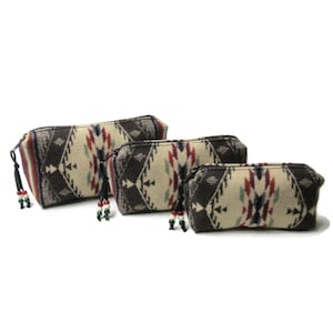 May include: Three different sized zippered pouches with a geometric pattern in shades of brown, beige, red, and green. Each pouch has a tassel with beads.