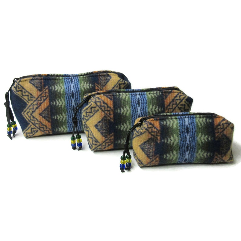 May include: Three different sized zippered pouches with a geometric pattern in shades of blue, green, brown, and black. The pouches have black zipper pulls and beaded tassels.