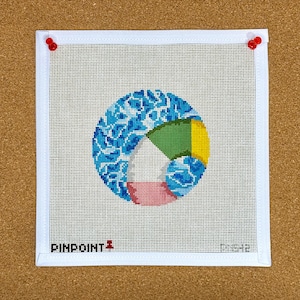 May include: A square needlepoint canvas with a geometric design in blue, green, yellow, and pink. The design is pinned to a corkboard with red push pins. The text "PINPOINT" is visible at the bottom.