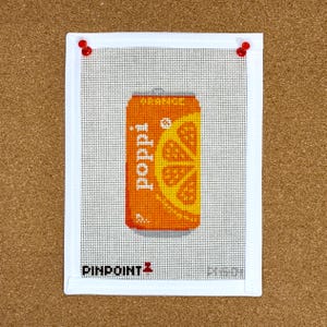 May include: A white canvas with a needlepoint design of an orange soda can with the word "Poppi" on it. The can is orange with a slice of orange on the front. The canvas has the words "PINPOINT" and a logo in the bottom left corner.