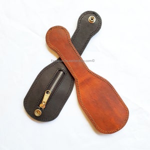 May include: Two leather paddles, one black and one brown, are displayed against a white background. The black paddle has a zippered pouch. Both paddles have a handle with a snap closure and are stitched around the edges.