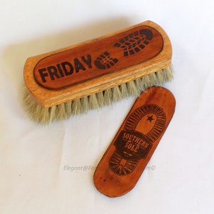 Könnte beinhalten: Eine Holzschuhbürste mit dem Wort "FRIDAY" und einem Fußabdruck-Design, neben einem kleinen, holzförmigen Gegenstand in Form einer Schuhsohle mit dem Text "SOUTHERN SOLE" und einem Stern. Die Bürste hat hellfarbene Borsten.