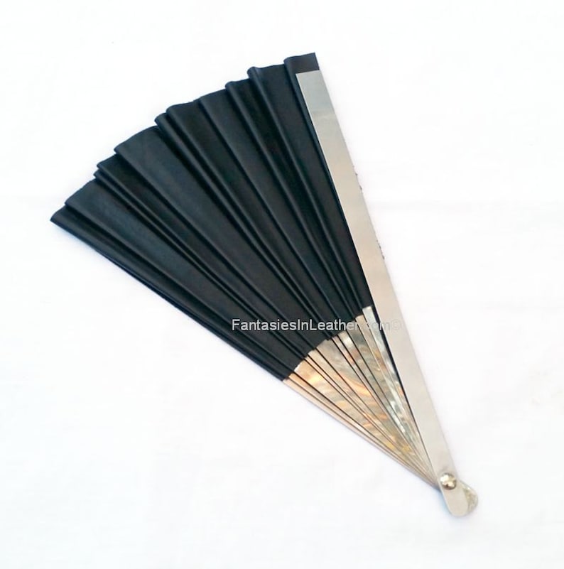 May include: A black hand fan with a silver metal handle and accents. The fan is made of pleated black material and is fanned out. The text "FantasiesInLeather" is printed on the fan.