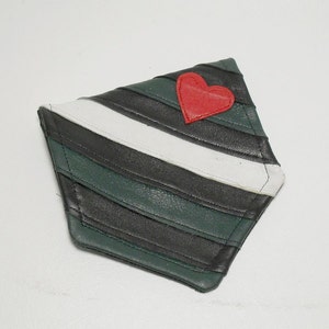 May include: A diamond-shaped leather item with a red heart applique. The item features alternating stripes of black, white, and green. The edges are stitched with white thread. The item is likely a decorative patch or accessory.