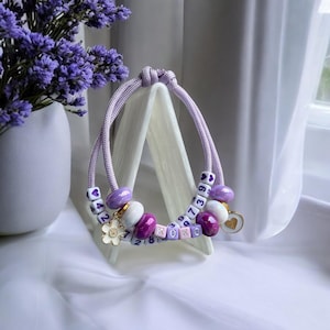 May include: A purple and white beaded bracelet with a flower charm and the numbers 42, 7, 2, 8, 9, 6, 3, 7 and the letters XOXO.