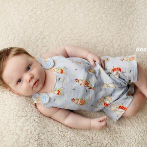 May include: A baby wearing a light blue and white patterned onesie with a button closure. The onesie has a variety of animal and floral designs. The baby is lying on a white fluffy surface.