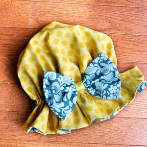 May include: A yellow fabric shower cap with white polka dots and a blue floral bow.