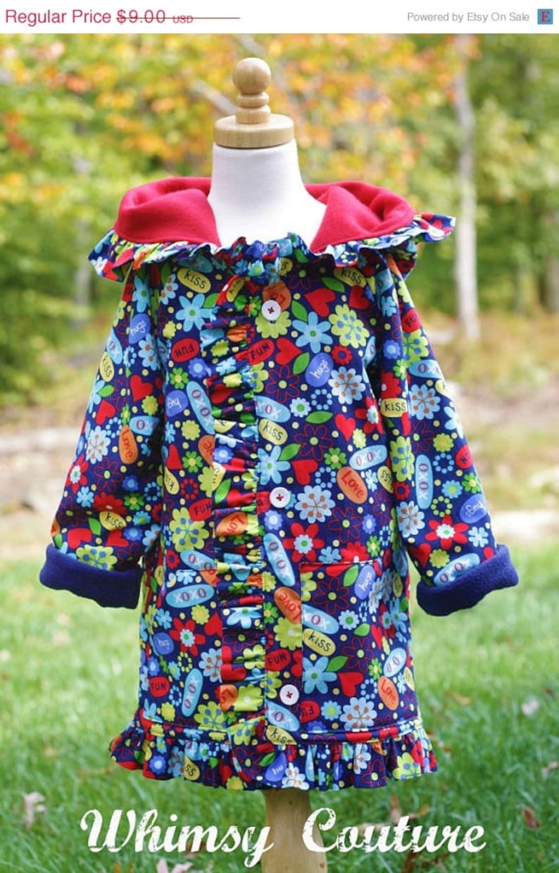 May include: A blue hooded jacket with a red fleece lining and a ruffle trim. The jacket is covered in a colorful print of flowers, hearts, and words like "kiss", "hugs", and "fun".