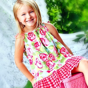 May include: A young girl wearing a pink and green floral dress with a pink polka dot ruffle. She is sitting on a pink wicker chair.
