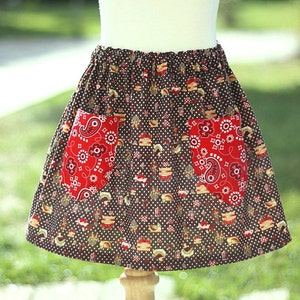 May include: A brown skirt with a white polka dot pattern and two red bandana pockets. The skirt is made of cotton fabric and has a gathered waist.
