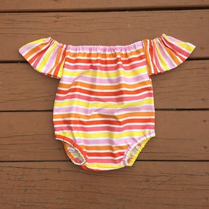 May include: A striped off-the-shoulder baby onesie with ruffled sleeves in shades of pink, yellow, orange, and red.