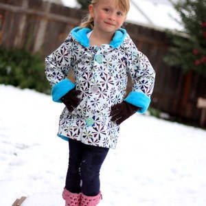 May include: A young girl wearing a white and black patterned jacket with blue trim and pink boots. She is standing in the snow.