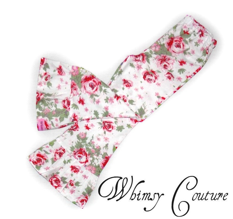 May include: White fabric with a floral pattern of red roses and green leaves. The fabric is folded and sewn into a scarf or headband shape. The text "Whimsy Couture" is written in cursive at the bottom right.