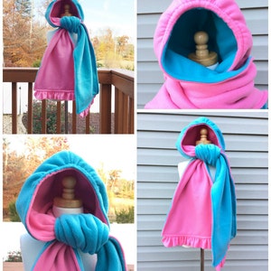 May include: A reversible hooded scarf with a pink and turquoise fleece fabric. The scarf can be worn with either side facing out.
