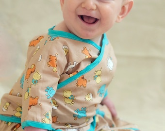 May include: A smiling baby wearing a tan and turquoise wrap-style onesie with a pattern of cartoon animals. The onesie has a turquoise trim.