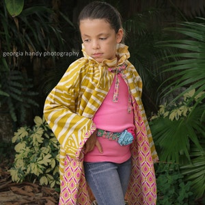 May include: A young person wearing a yellow and white striped jacket with a pink and white floral pattern on the bottom. The jacket has a pink ruffled collar and a pink and white floral belt. The person is wearing blue jeans and a pink shirt.
