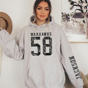May include: A light gray Warhawks hoodie with the number 58 in distressed black font on the front. The name "Jackson" is printed vertically on the left sleeve in black. The hoodie has a drawstring hood.