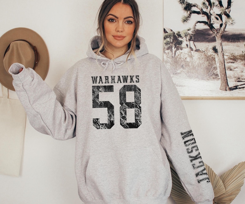 May include: A light gray Warhawks hoodie with the number 58 in distressed black font on the front. The name "Jackson" is printed vertically on the left sleeve in black. The hoodie has a drawstring hood.